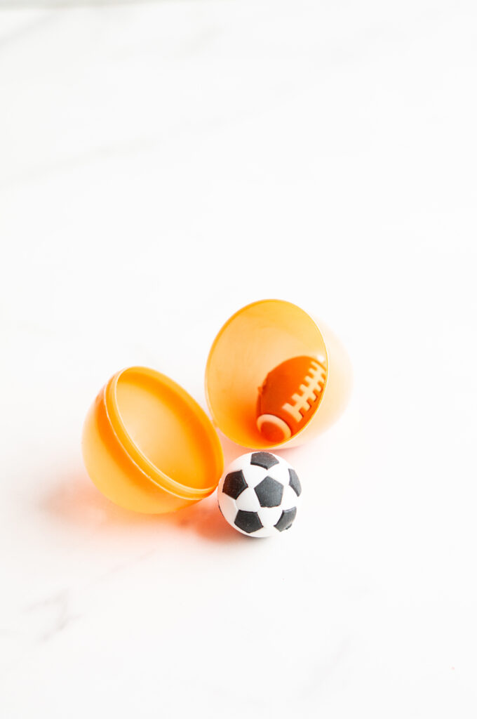 This image shows a plastic easter egg filled with non candy item of sports erasers.