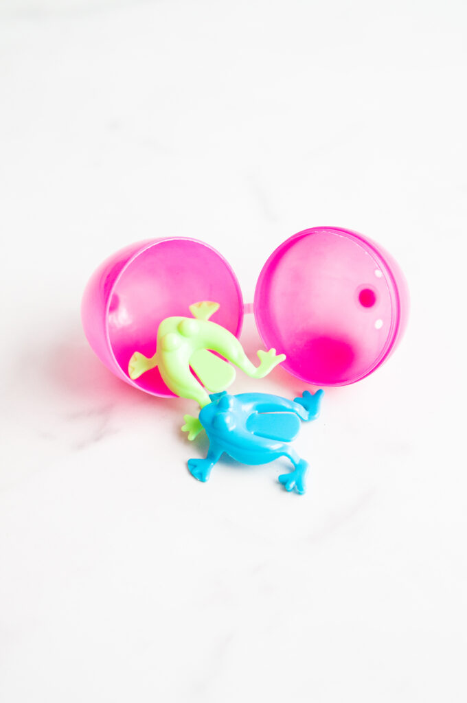 This image shows a plastic easter egg filled with non candy item of frog jumpers.