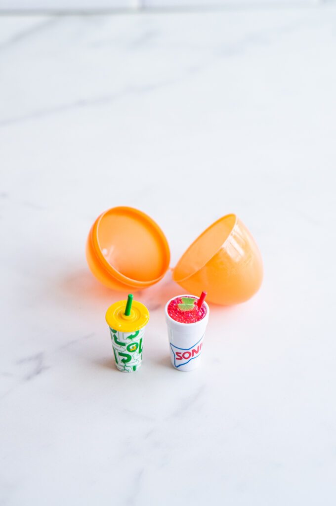 This image shows a plastic easter egg filled with non candy item of 2 mini brands drinks.