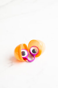 This image shows a plastic easter egg filled with non candy item of googly eye ring.