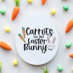 This image shows an egg shaped plate with the words Carrots for the Easter Bunny on it. It is surrounded by small color eggs and faux carrots.