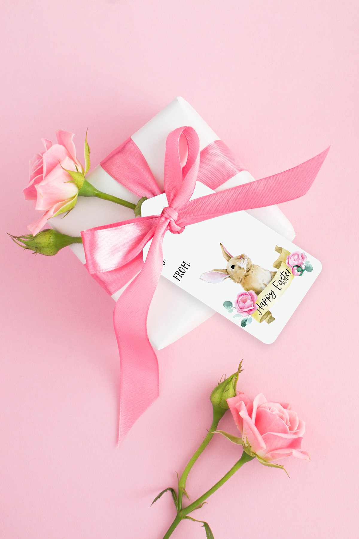 One of the free pretty Easter gift tags is attached to a wrapped gift with a large pink bow and pink carnation sticking out of it. There is an additional pink carnation at the bottom of the image.