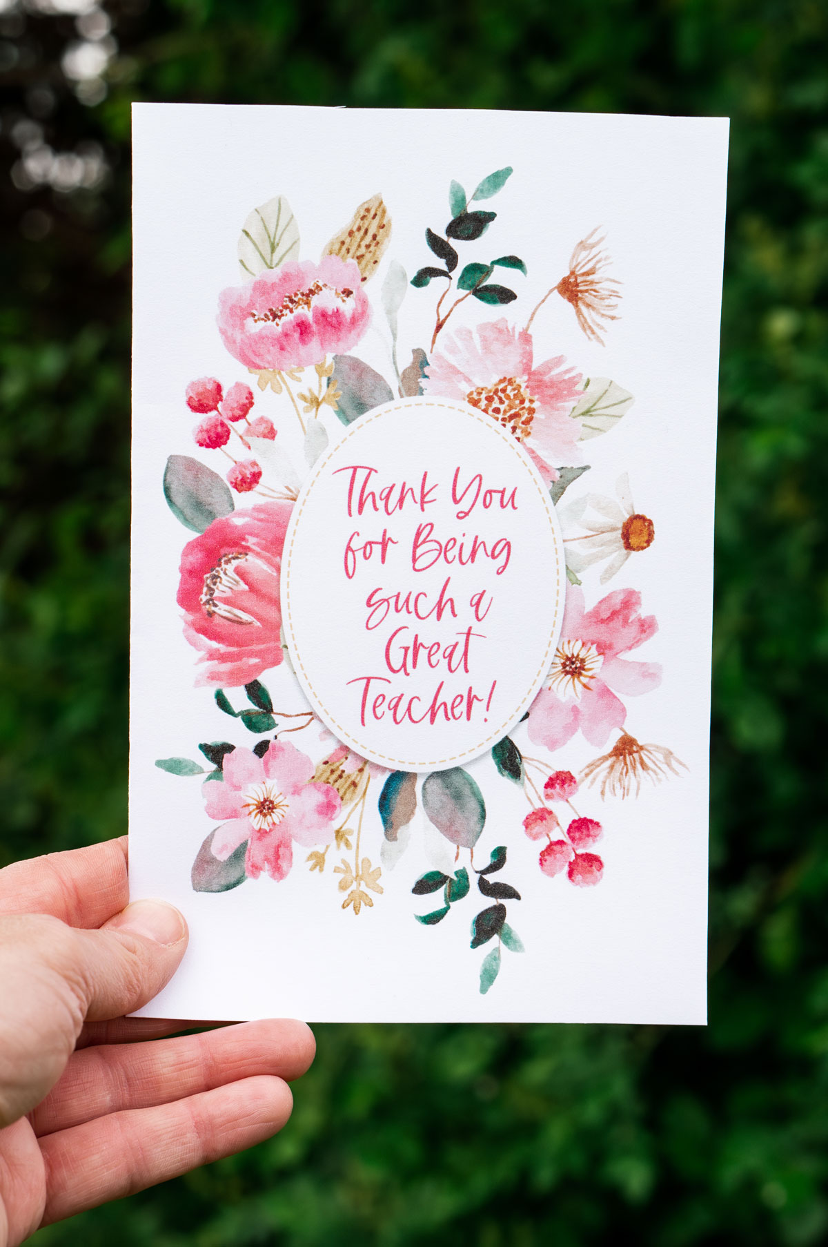 This image is of someone holding one of the free printable thank you cards for teacher appreciation or the end of the year. It says thank you for being a great teacher! and is surrounded by beautiful flowers in shades of pink.