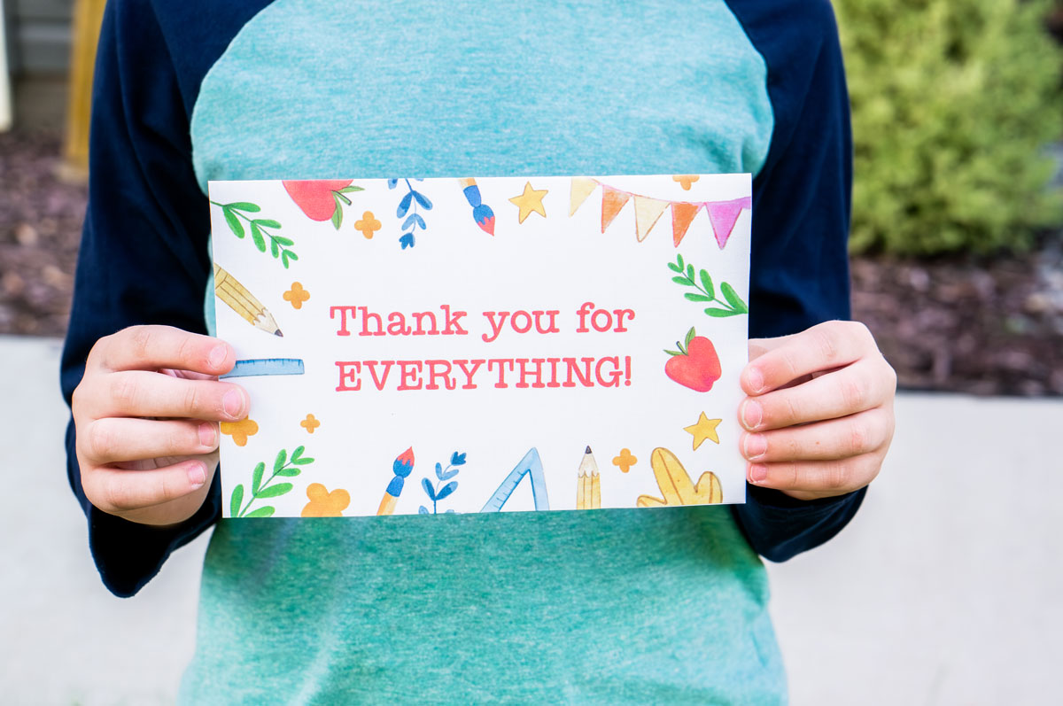 This image is of a child holding one of the free printable thank you cards for teacher appreciation or the end of the year. It says thank you for everything! and is surrounded by a border of school supplies.