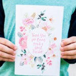 This image is of a child holding one of the free printable thank you cards for teacher appreciation or the end of the year. It says thank you for being a great teacher! and is surrounded by beautiful flowers in shades of pink.