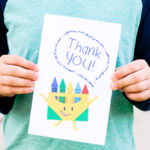 This image is of a child holding one of the free printable thank you cards for teacher appreciation or the end of the year. It has a pack of crayons that is saying thank you!