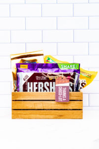 This image shows a wooden crate filled with various types of chocolate and a chocolate themed gift tag that says, Thanks choco-lot.