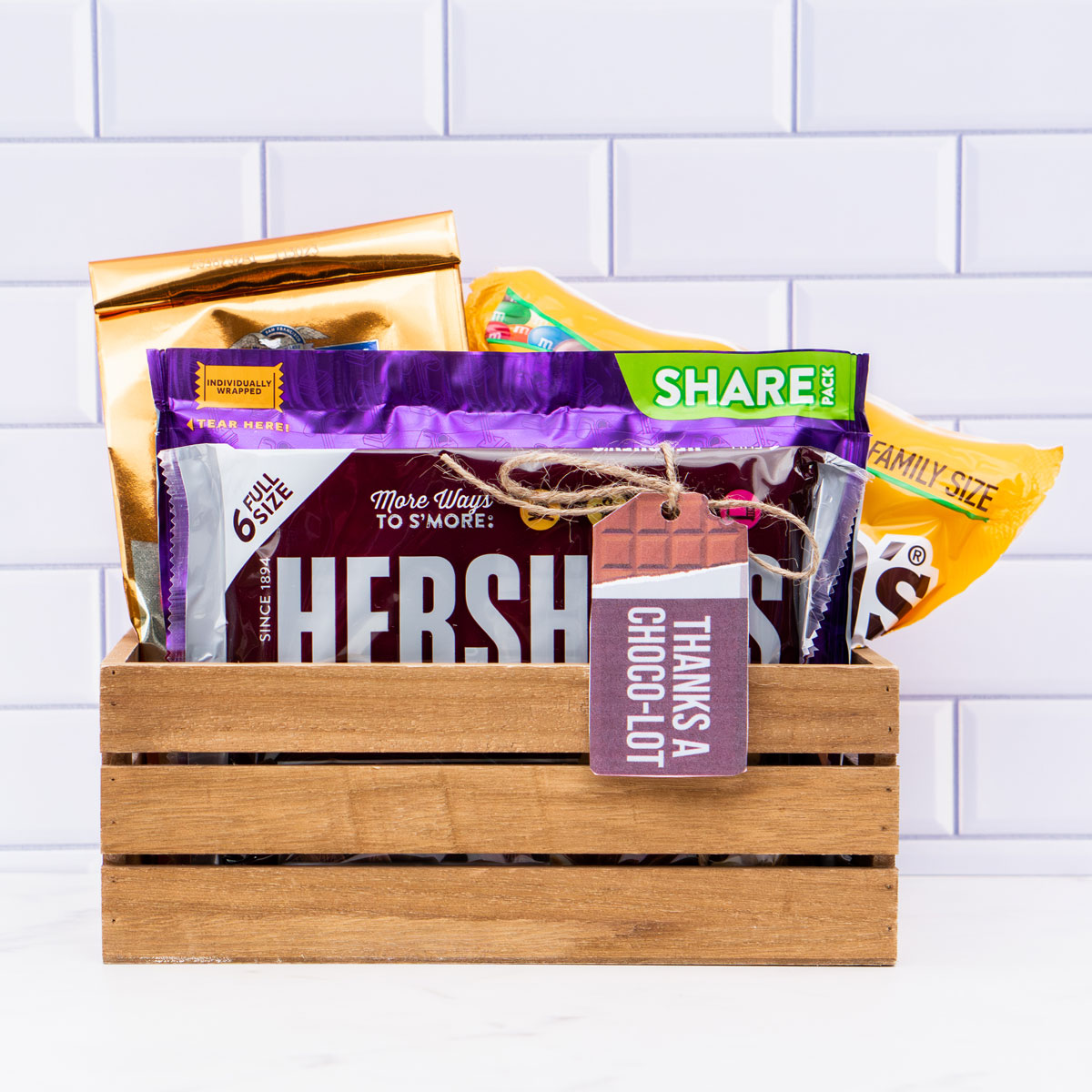 This image shows a wooden crate filled with various types of chocolate and a chocolate themed gift tag that says, Thanks choco-lot.