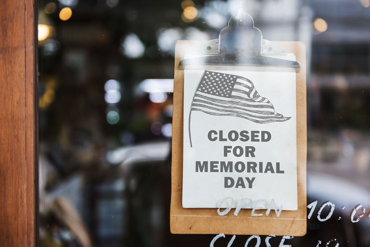 This image shows a free printable Closed for Memorial Day sign with a black and white American flag on the top left corner.