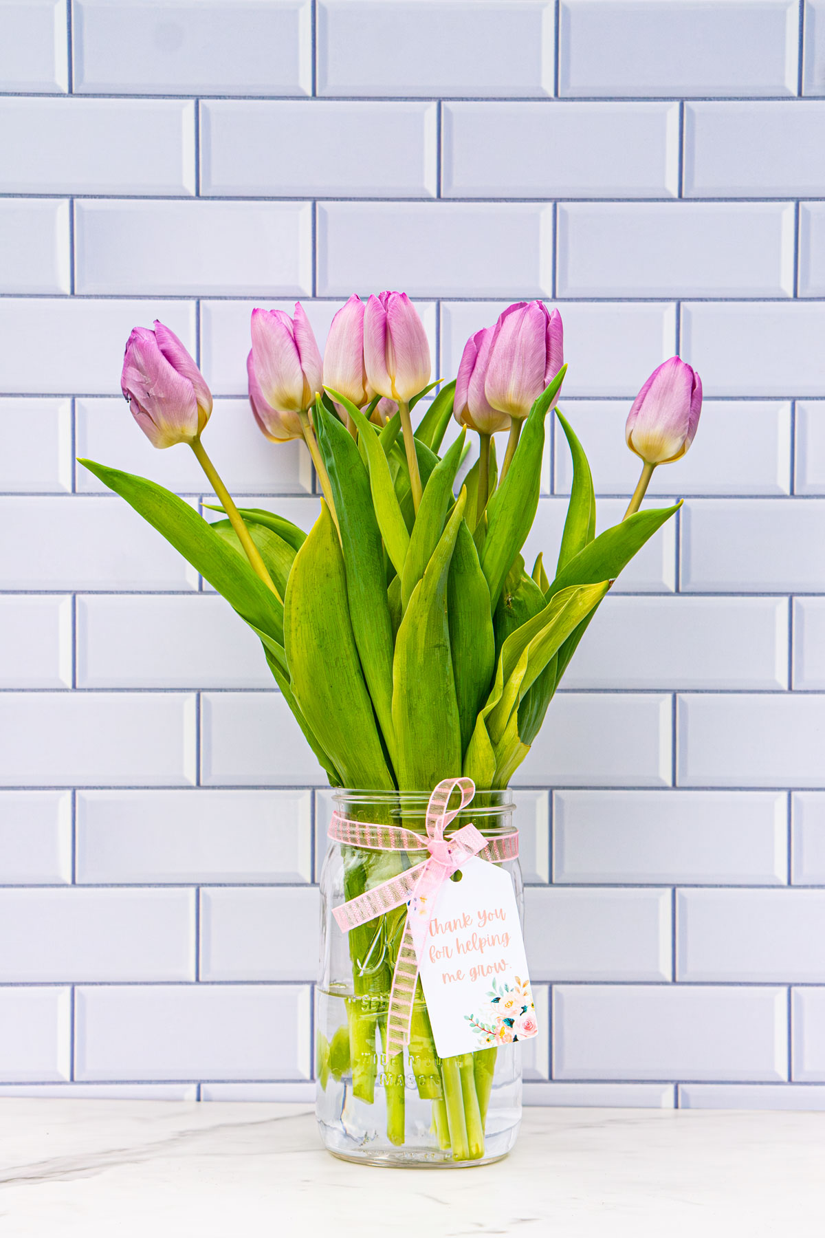 This image is of a mason jar of flowers (purple tulips) with a gift tag that says, "Thanks for helping me grow."