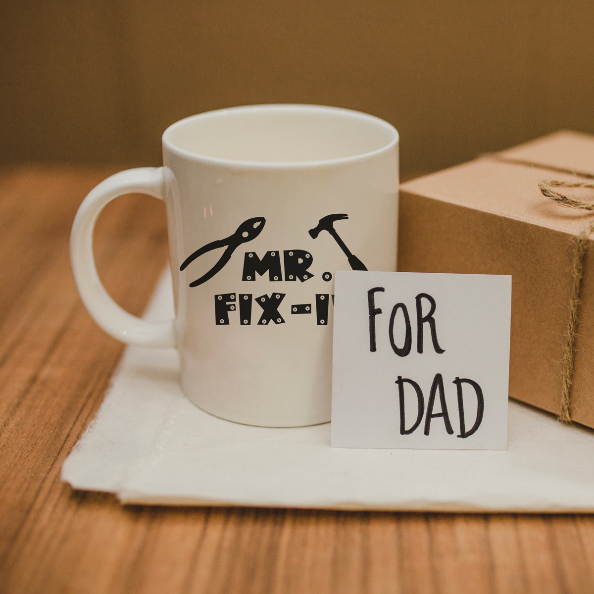 This image shows a mug that says Mr. Fix-It (although the it is covered up). In front of the mug is a small card that says for Dad.