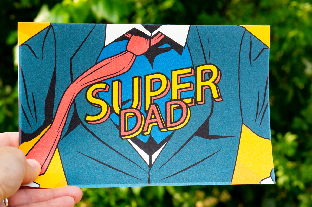 This is a picture of a card that says Super Dad across the chest of a man in a suit open to a superhero costume.