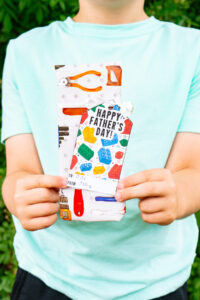This image shows a boy holding a wrapped present with a gift tag that says Happy Fathers Day with legos that you can get from the free Happy Fathers Day tags printable set at the end of this post.