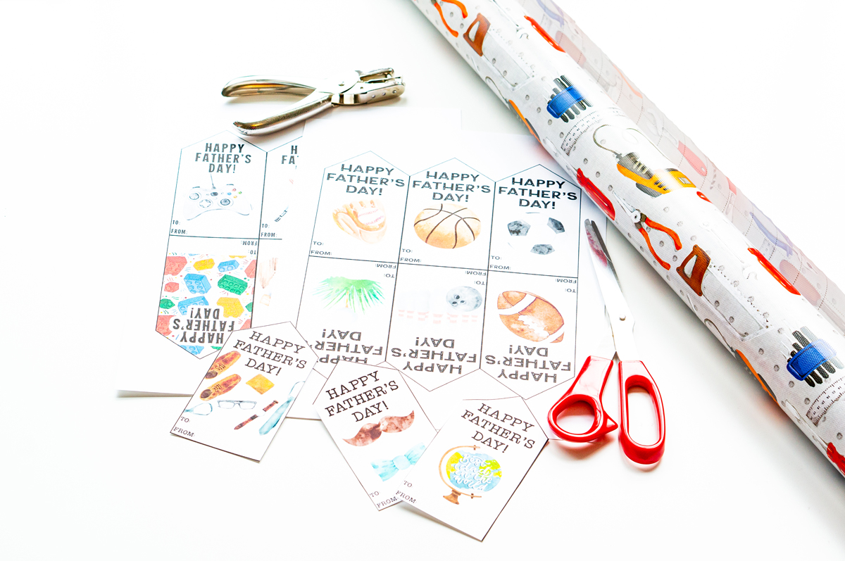 This image shows some tool themed wrapping paper, a hole punch, scissors, and some Happy Fathers Day tags printables you can get for free at the end of this post.