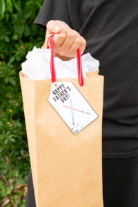 This image shows a boy holding a gift bag with a gift tag that says Happy Fathers Day with 2 light sabers that you can get from the free Happy Fathers Day tags printable set at the end of this post.