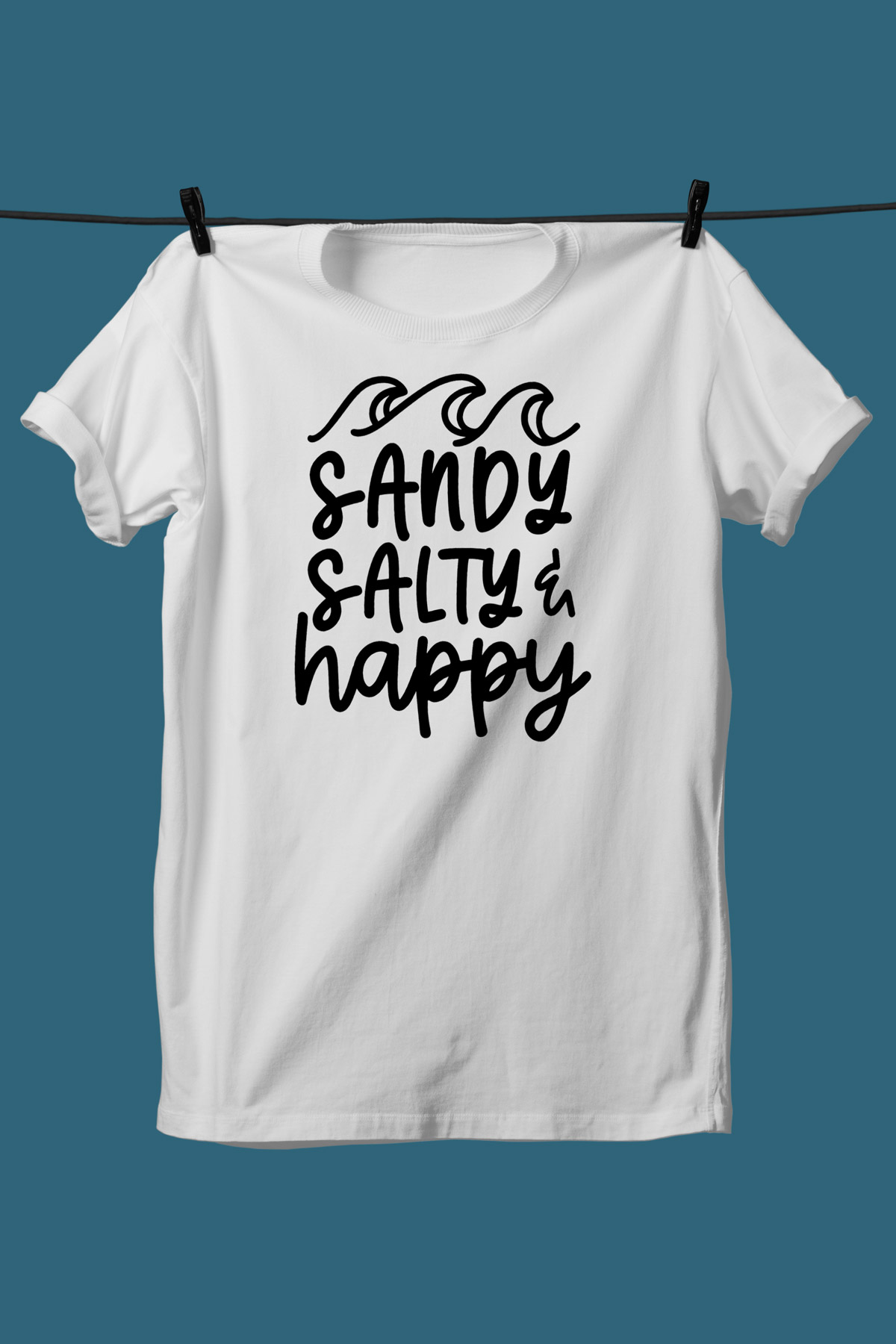 This image shows one of the SVGs from the free summer SVG set on a white tshirt. This one says sandy, salty, & happy with some waves on top.