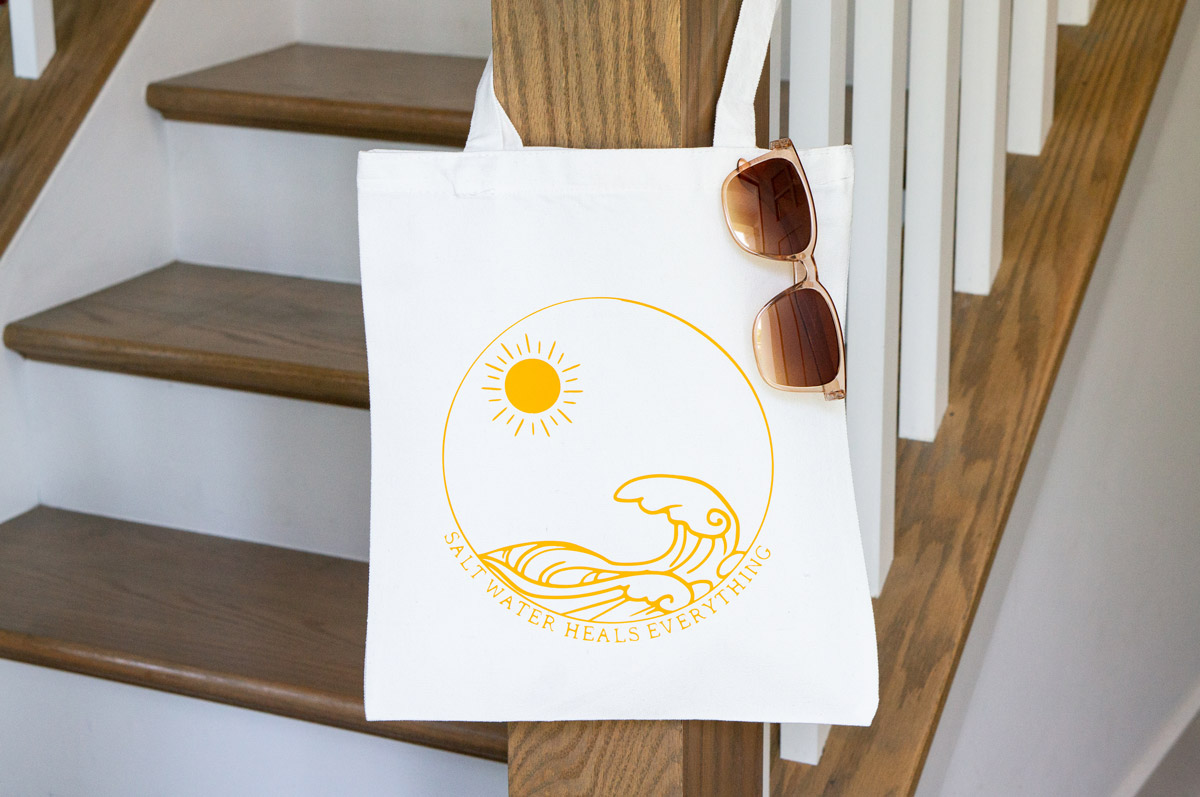 In this image, it shows one of the SVGs from the free summer SVG set. This one says salt water heals everything with the picture of waves and the sun on a tote bag.