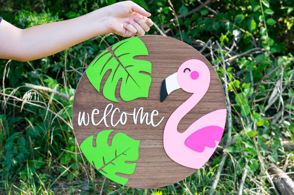 This image shows the completed layered wood sign with the free summer welcome sign SVG file. It is a flamingo, two tropical leaves, and the word welcome.