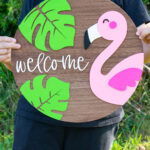 This image shows the completed layered wood sign with the free summer welcome sign SVG file. It is a flamingo, two tropical leaves, and the word welcome.