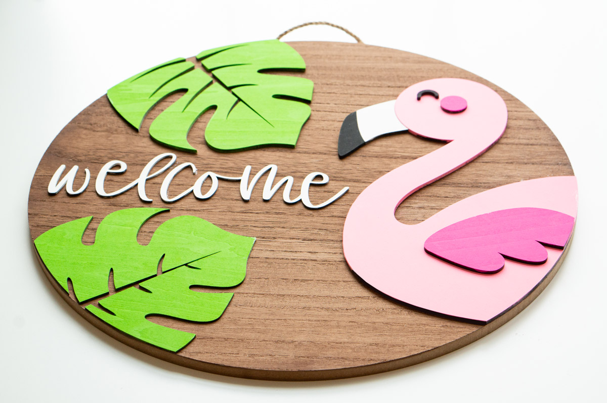 This image shows the completed layered wood sign with the free summer welcome sign SVG file. It is a flamingo, two tropical leaves, and the word welcome.