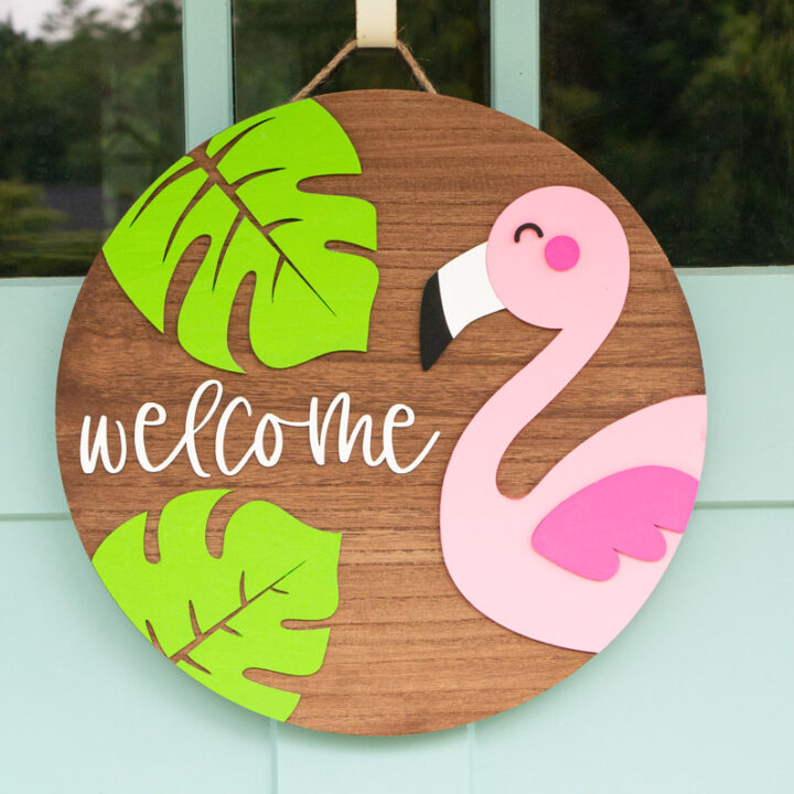 This image shows the completed layered wood sign with the free summer welcome sign SVG file. It is a flamingo, two tropical leaves, and the word welcome.