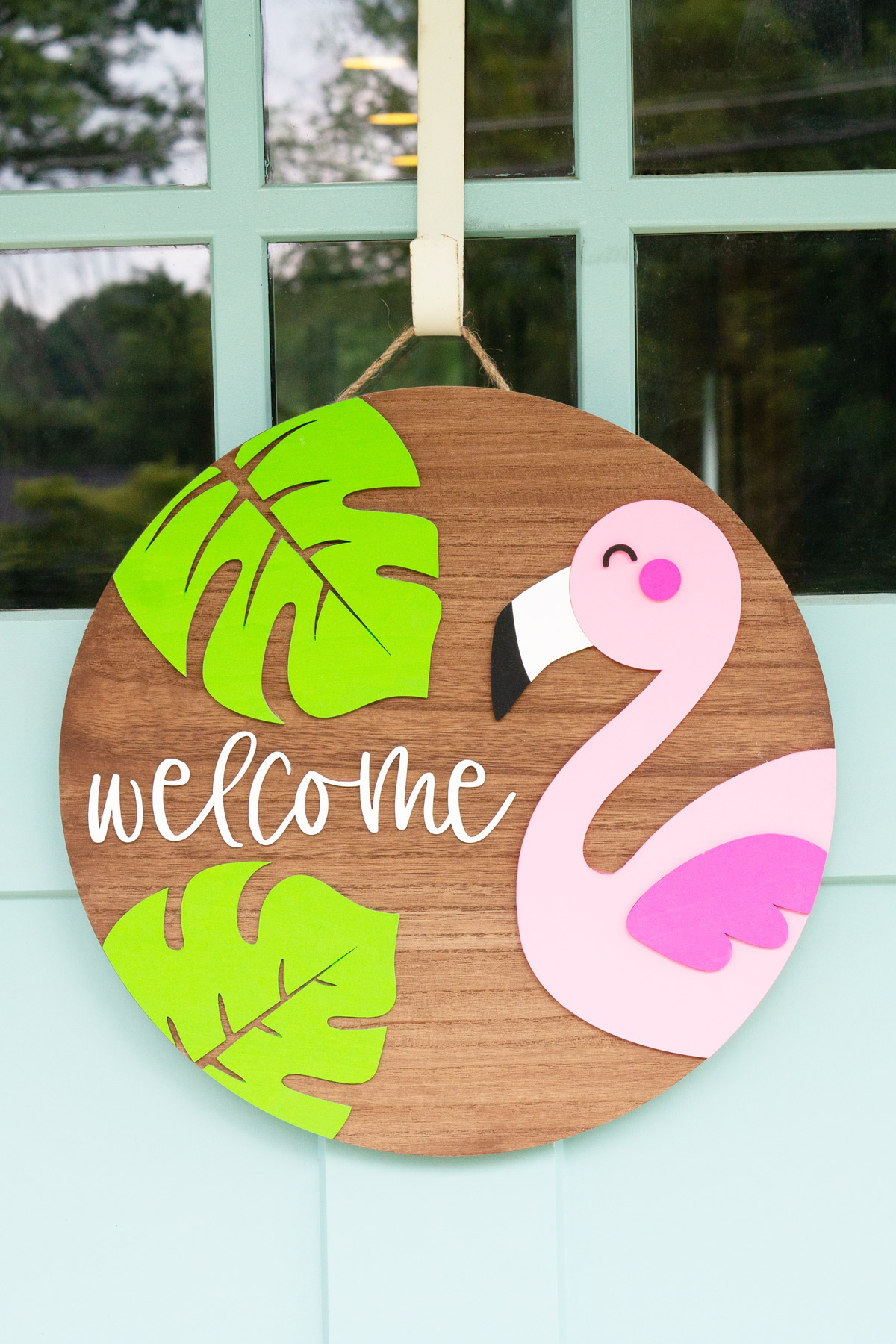 This image shows the completed layered wood sign with the free summer welcome sign SVG file. It is a flamingo, two tropical leaves, and the word welcome.