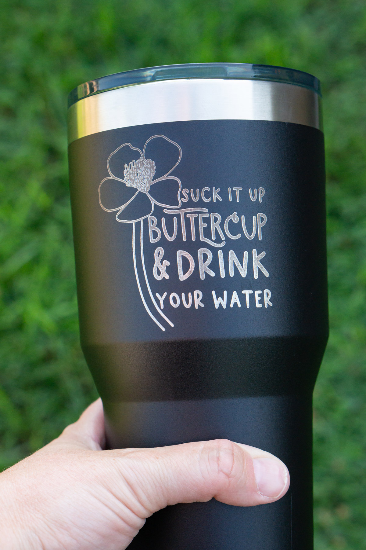 The image is of a laser engraved tumbler that says suck it up buttercup and drink your water - with the drawing of a buttercup flower.