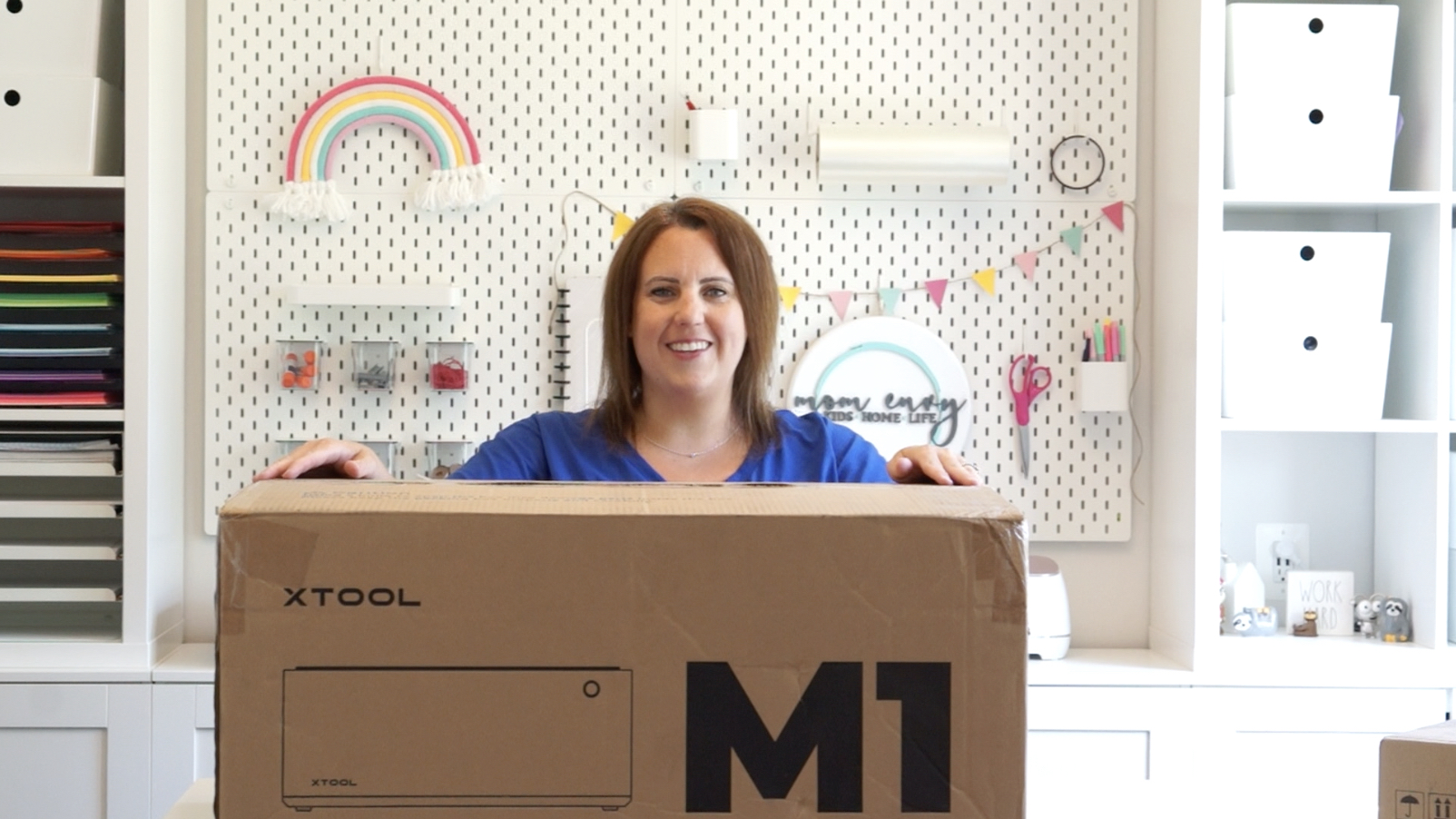 This image is showing a woman in a craft room standing behind the xTool M1 machine (which is a hybrid laser and cutting machine).