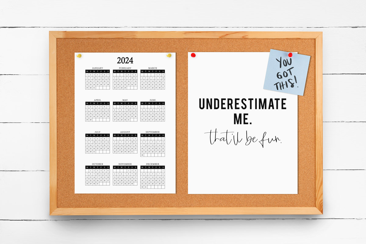 This image shows a 2024 free printable year at a glance calendar you can get for free in this blog post. The calendar is hanging on a bulletin board next to a print that says underestimate me, that'll be fun and a post it note that says you got this!