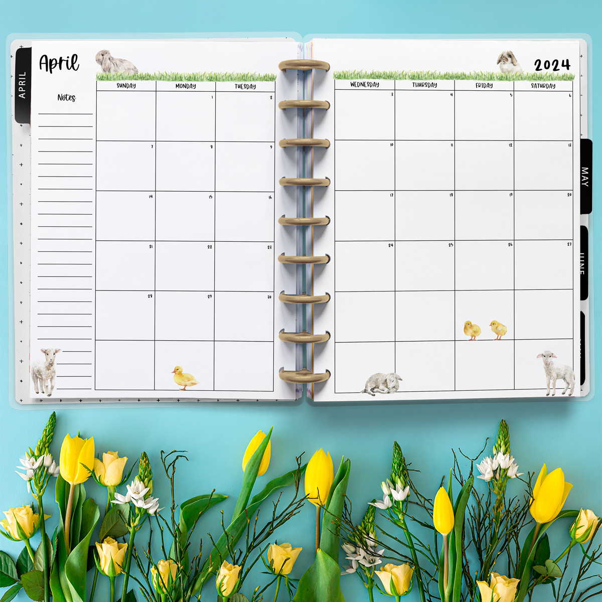 This image is an example of one of the printable 2024 calendar you can get for free at the end of this post. This is showing the month of April inside of an open planner with some flowers below the planner.