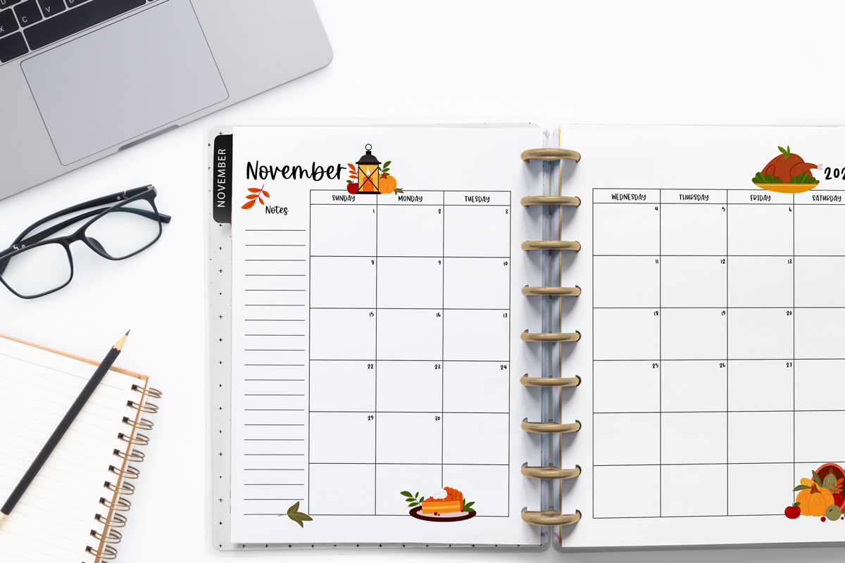 This image is an example of one of the printable 2026 calendar you can get for free at the end of this post. This is showing the month of November inside of an open planner. Above the planner is an open laptop keyboard, some paper, a pencil, and a pair of glasses.