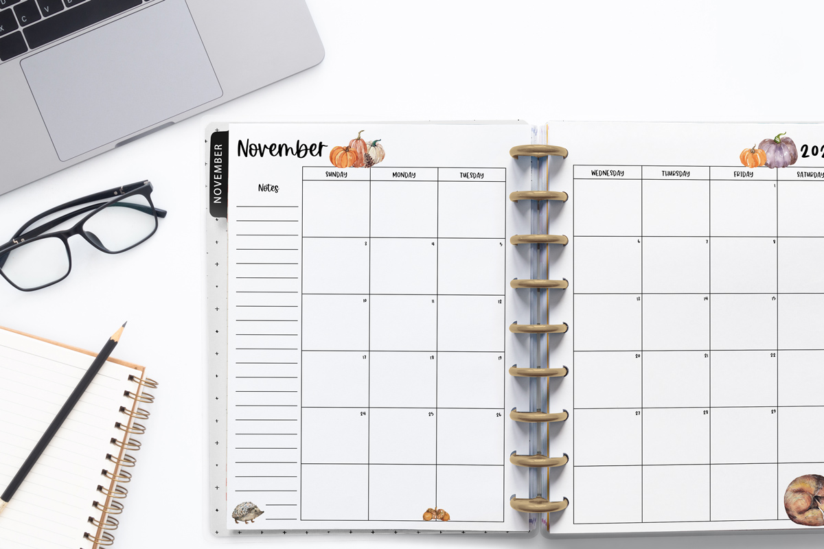 This image is an example of one of the printable 2024 calendar you can get for free at the end of this post. This is showing the month of November inside of an open planner. Above the planner is an open laptop keyboard, some paper, a pencil, and a pair of glasses.