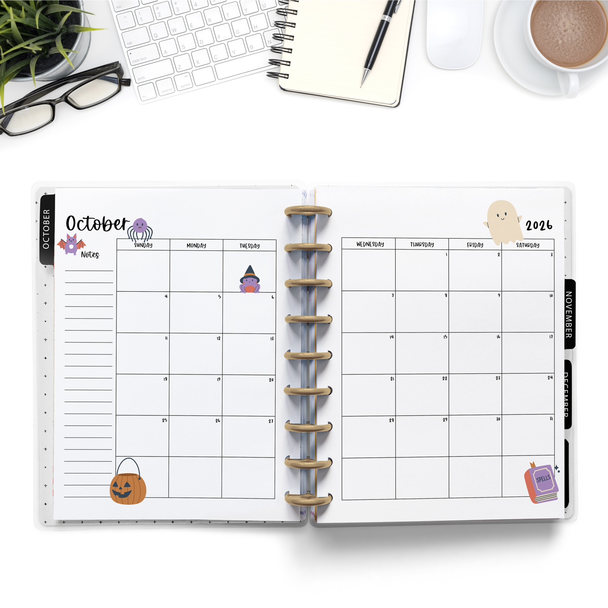 This image is an example of one of the printable 2026 calendar you can get for free at the end of this post. This is showing the month of October inside of an open planner. Above the planner is an open laptop keyboard, a notebook, a pencil, cup of coffee, a plant, and a pair of glasses.
