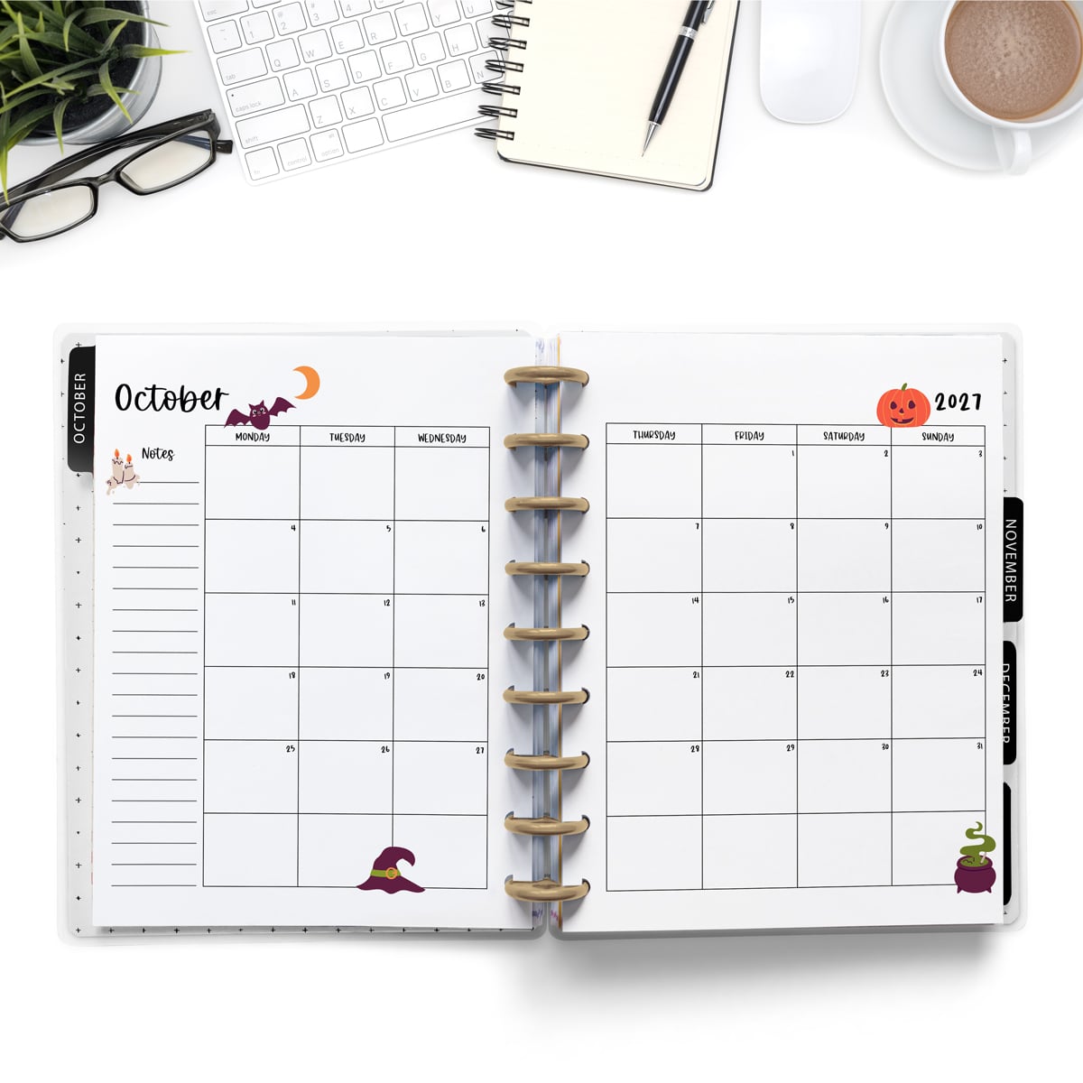 This image is an example of one of the printable 2027 calendar you can get for free at the end of this post. This is showing the month of October inside of an open planner. Above the planner is an open laptop keyboard, a notebook, a pencil, cup of coffee, a plant, and a pair of glasses.