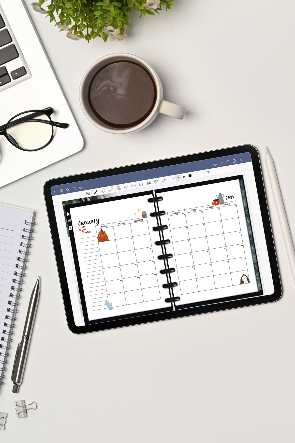 This image is an example of one of the printable and digital 2025 calendar you can get for free at the end of this post. This is showing the month of January inside of an open digital planner on an iPad. Above the tablet is a cup of coffee, some glasses, a notebook and pen, part of a laptop computer, and part of a plant.