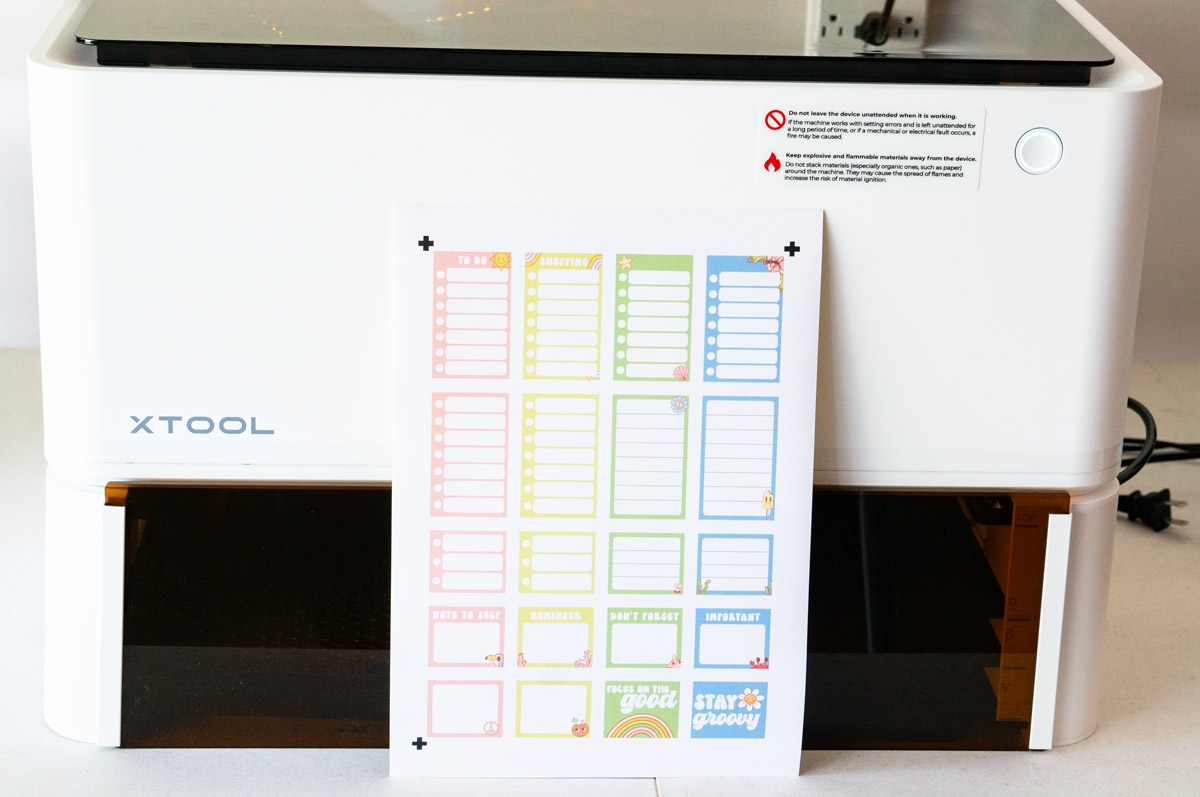 This is an image of the xTool M1 machine with a printed page of stickers leaning against it.