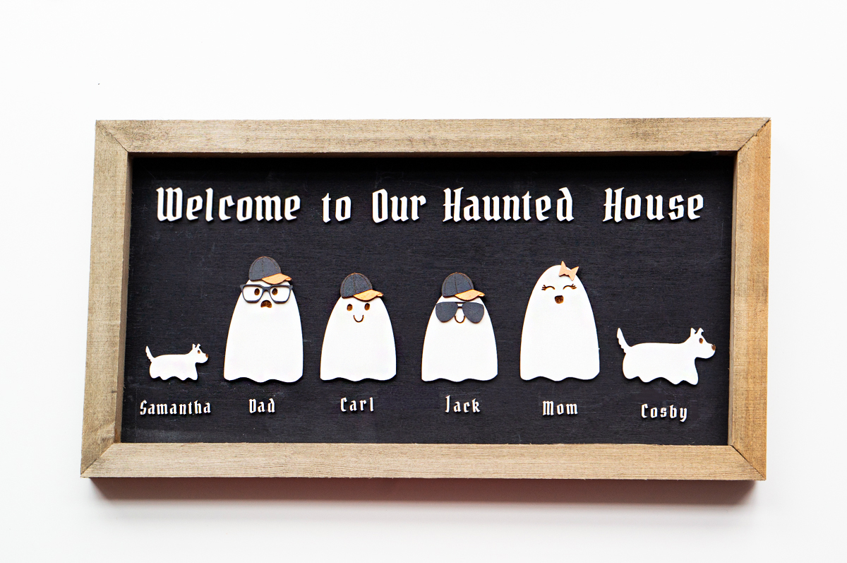 This image shows the completed example of the Halloween ghost family wood sign using the free ghost family SVG set. At the top it says welcome to our haunted house. Then there are some ghosts in the middle with the names, Samantha, Dad, Carl, Jack, Mom, and Cosby.