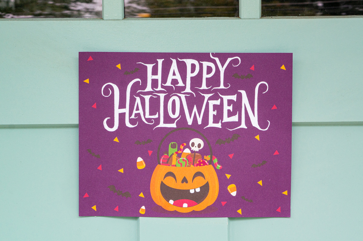 This image shows one of the free printable Halloween candy signs you can get in this free set. This sign is hanging on a door and says Happy Halloween!