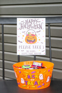 This image shows one of the free printable Halloween candy signs you can get in this free set. This sign says Happy Halloween. Please take 3. Be kind and leave some behind. Under the sign is a bowl of candy.