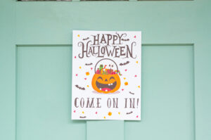 This image shows one of the free printable Halloween candy signs you can get in this free set. This sign is hanging on a door and says Happy Halloween come on in!