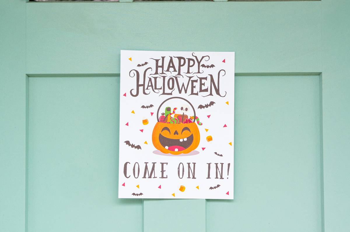 This image shows one of the free printable Halloween candy signs you can get in this free set. This sign is hanging on a door and says Happy Halloween come on in!