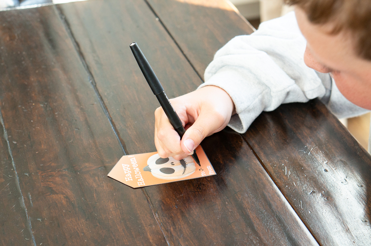 This image shows a child filling out one of the free Happy Halloween printable tags.