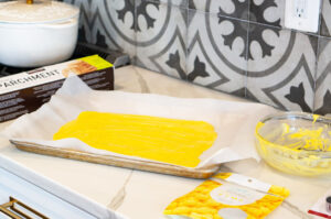 This image shows melted chocolate on parchment paper on a sheet pan in preparation for making butter to go on the Turkey Dinner cookie sets.