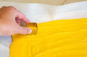 This image shows cutting out squares of the cooled melted chocolate on parchment paper on a sheet pan in preparation for making butter to go on the Turkey Dinner cookie sets.