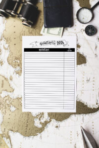 Adventures for 2026&rsquo; printable sheet laid on top of a vintage world map with travel accessories including binoculars, a wallet, cash, and a magnifying glass.