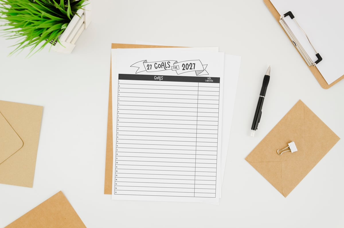 27 Goals for 2027 printable sheet sitting on a white desk with envelopes, clipboard, pen, and a small plant.