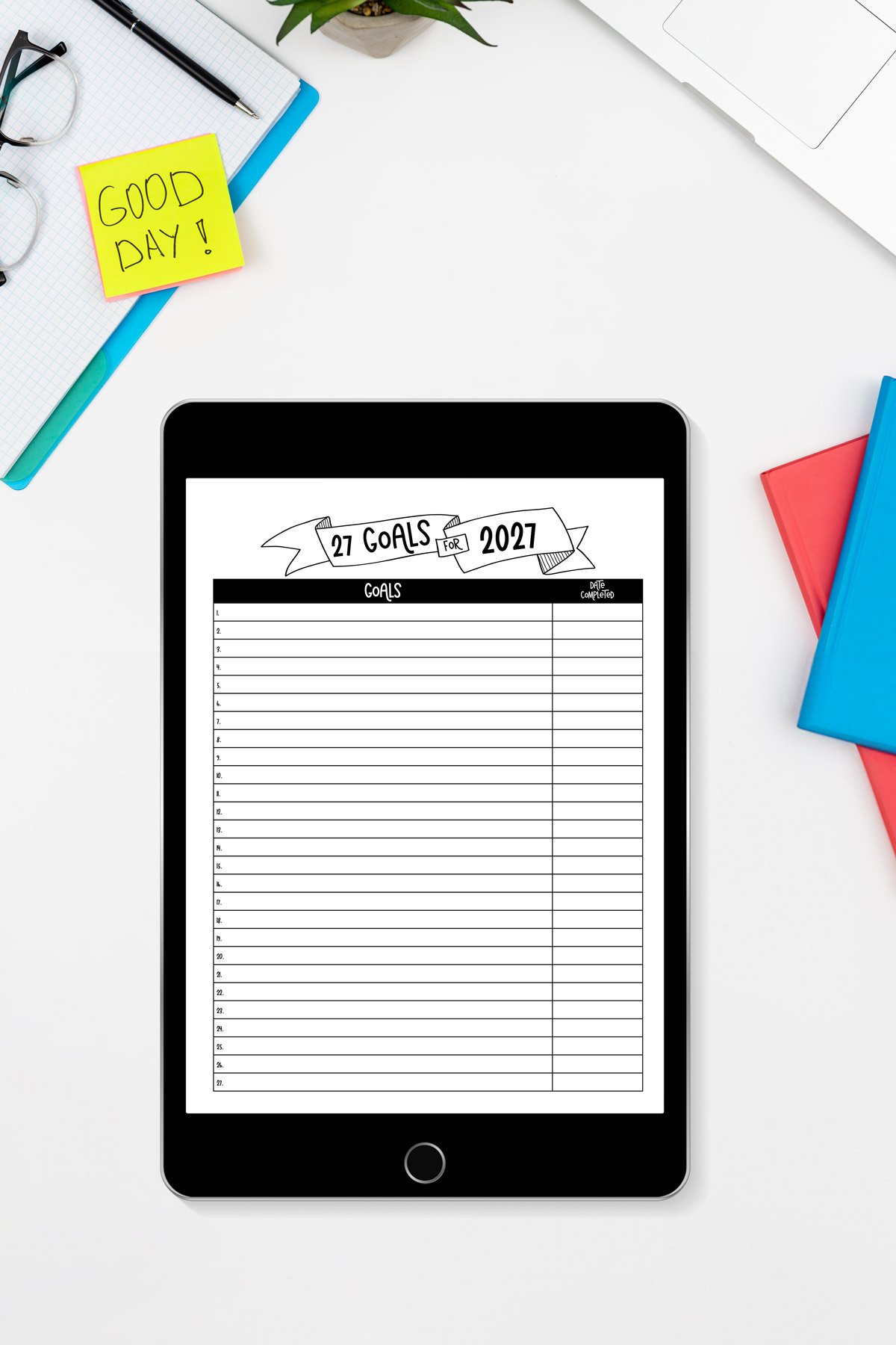 iPad displaying the '27 Goals for 2027' digital planner page on a white desk with glasses, sticky notes, books, and a plant.