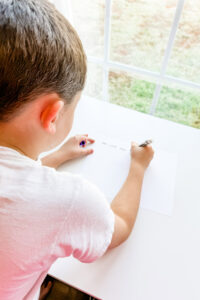 This image is of a chid writing a note to their grandma with a black marker on white paper. This writing will be used for a handwriting laser gift.