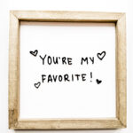 This image is showing a wood sign that has black acrylic cut out from an SVG of handwriting that says: you're my favorite! with hearts around it.