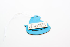 This is an example of one of the Easter basket tag SVG files completed using a laser machine to cut the wood. Here it's showing how the surround from the cut out of the name is being used like a stencil to place the letters in the name correctly.